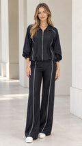 Front full view of woman wearing black tracksuit set with contrast white piping and wide leg pants