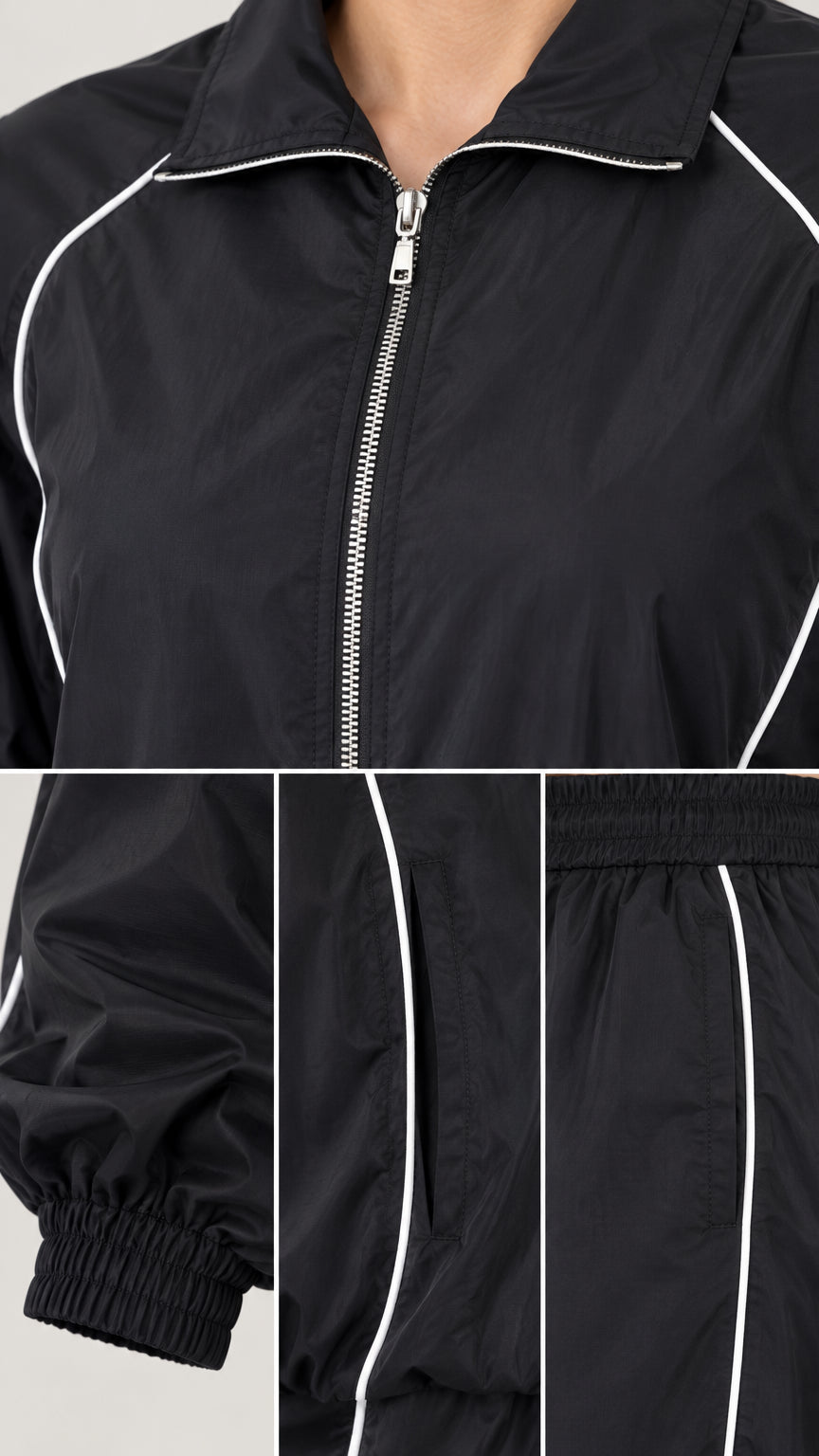 Close-up details of black zip jacket zipper, contrast piping trim, and elastic cuff